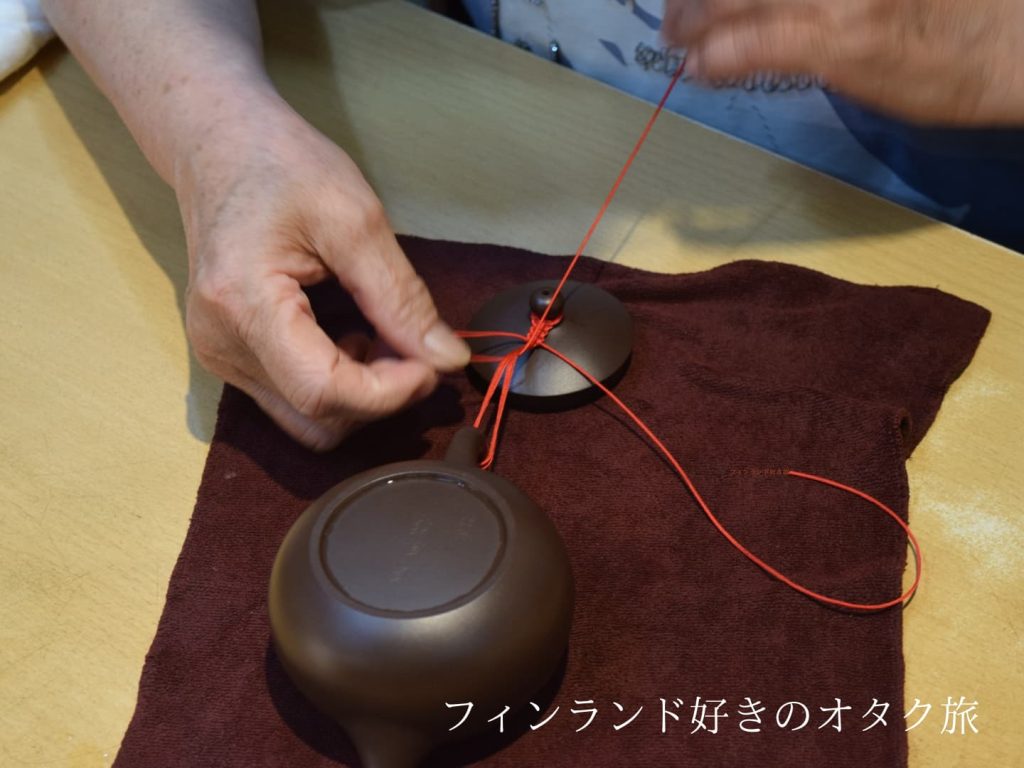 おばちゃんが茶壺の蓋と取手を紐で結びつけてくれる様子