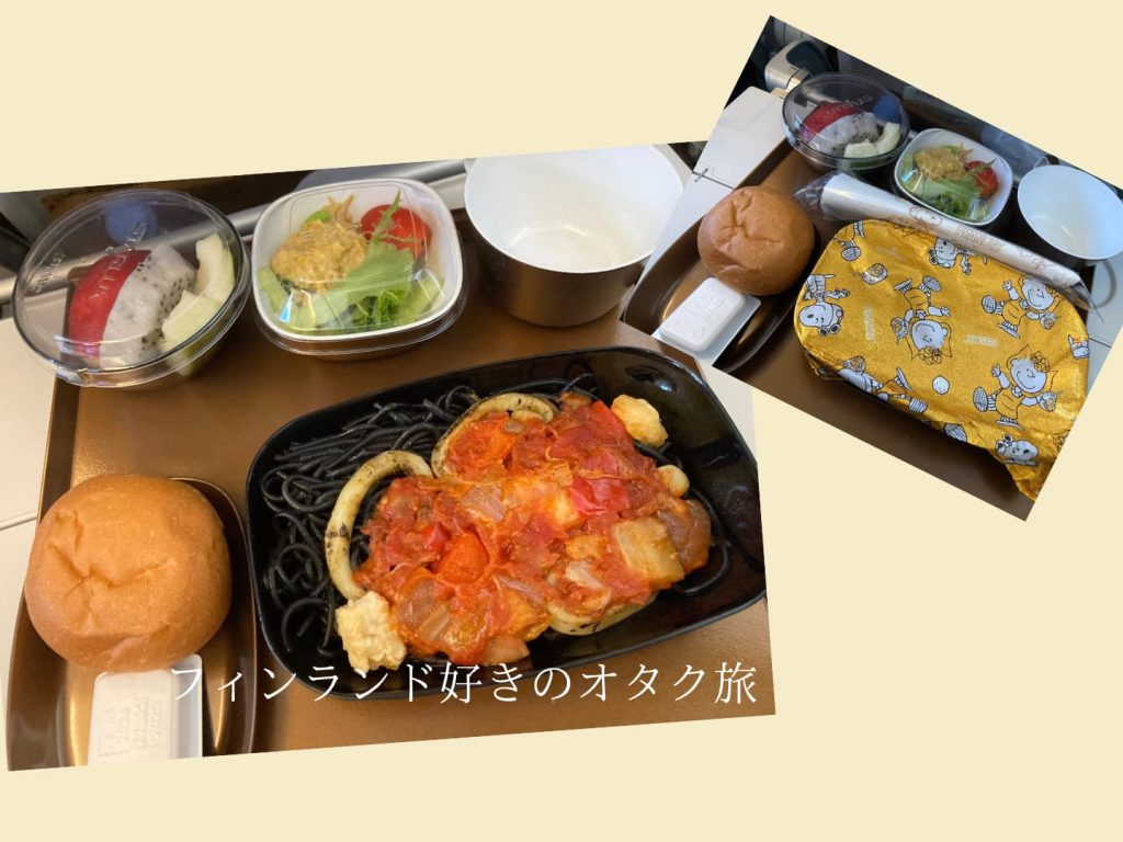 機内食。イカ墨パスタとフルーツとサラダとパン。パスタの蓋にはスヌーピーが描かれている